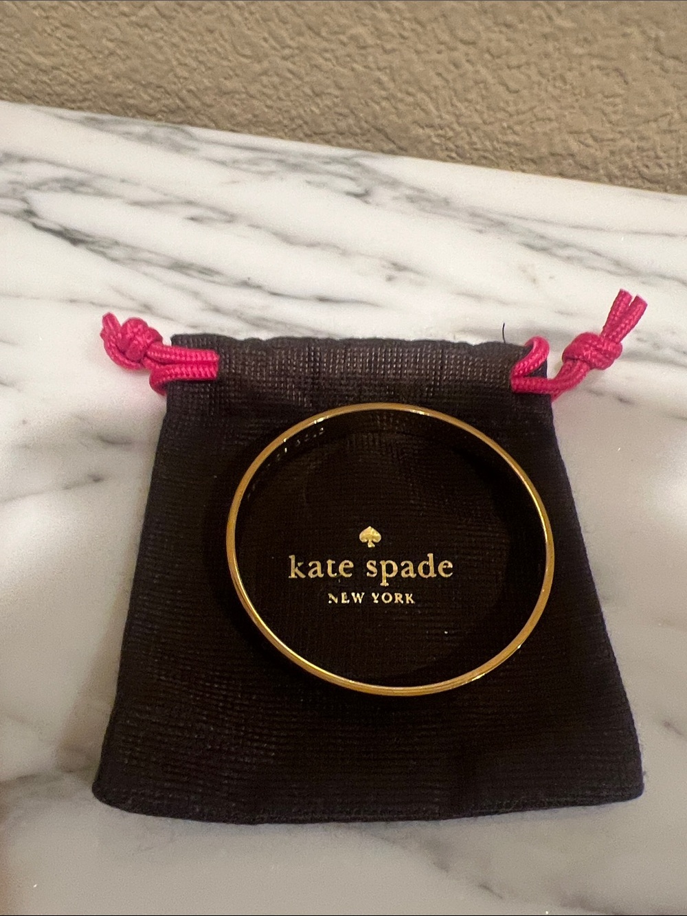 Kate Spade gold-tone bangle with brown  pouch and pink drawstrings